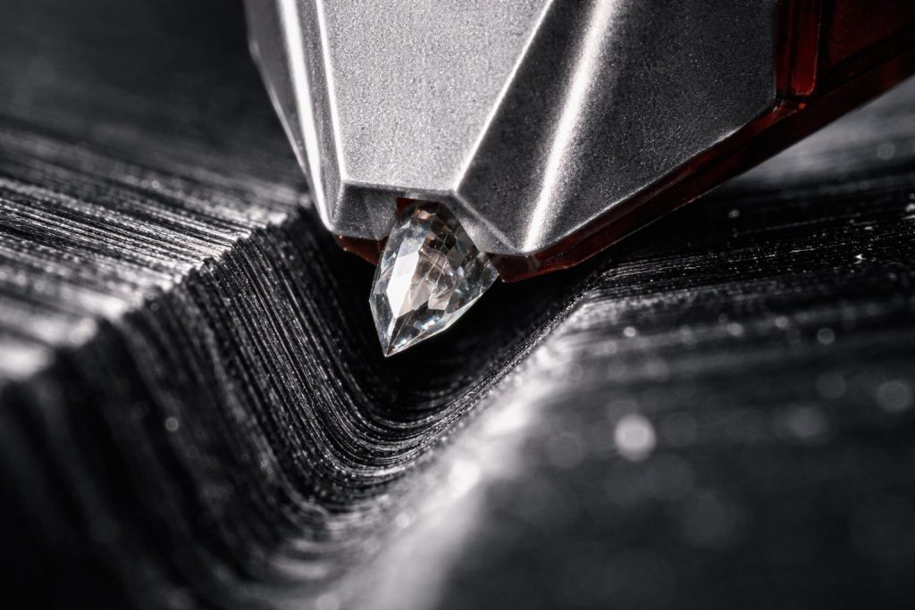 Macro fotografia estrema dello stilo di una testina hi-fi immerso nel solco del vinile, con evidenza del contatto tra diamante e pareti del solco per il corretto controllo di Tracking Force, VTA (Vertical Tracking Angle) e Stylus Rake Angle. L’immagine mostra il processo di fine-tuning dell’assetto analogico ad altissima precisione, contenuto tecnico realizzato per Fader Space.